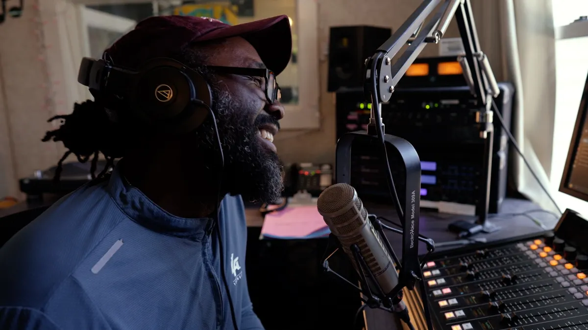 A black man sits in front of a microphone, smiling.