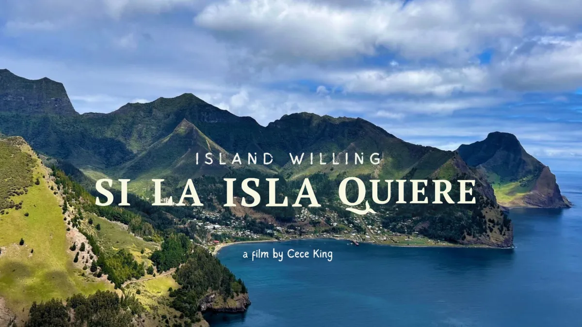 A volcanic archipelago is vividly green and surrounded by blue ocean. Nestled in the middle is a small town. Text overlays the image. The biggest in the middle says "SI LA ISLA QUIERE" with the English translation "Island Willing" above and "Film by Cece King" below.