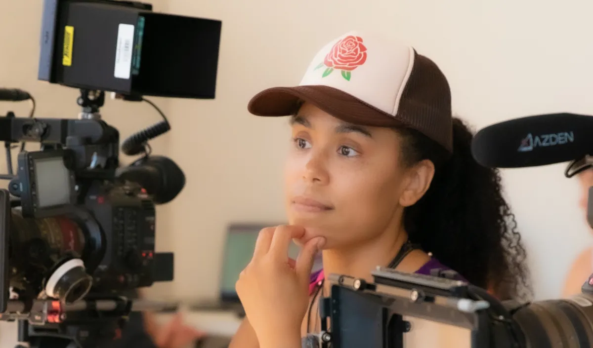 Black woman with a trucker hat looks through a camera