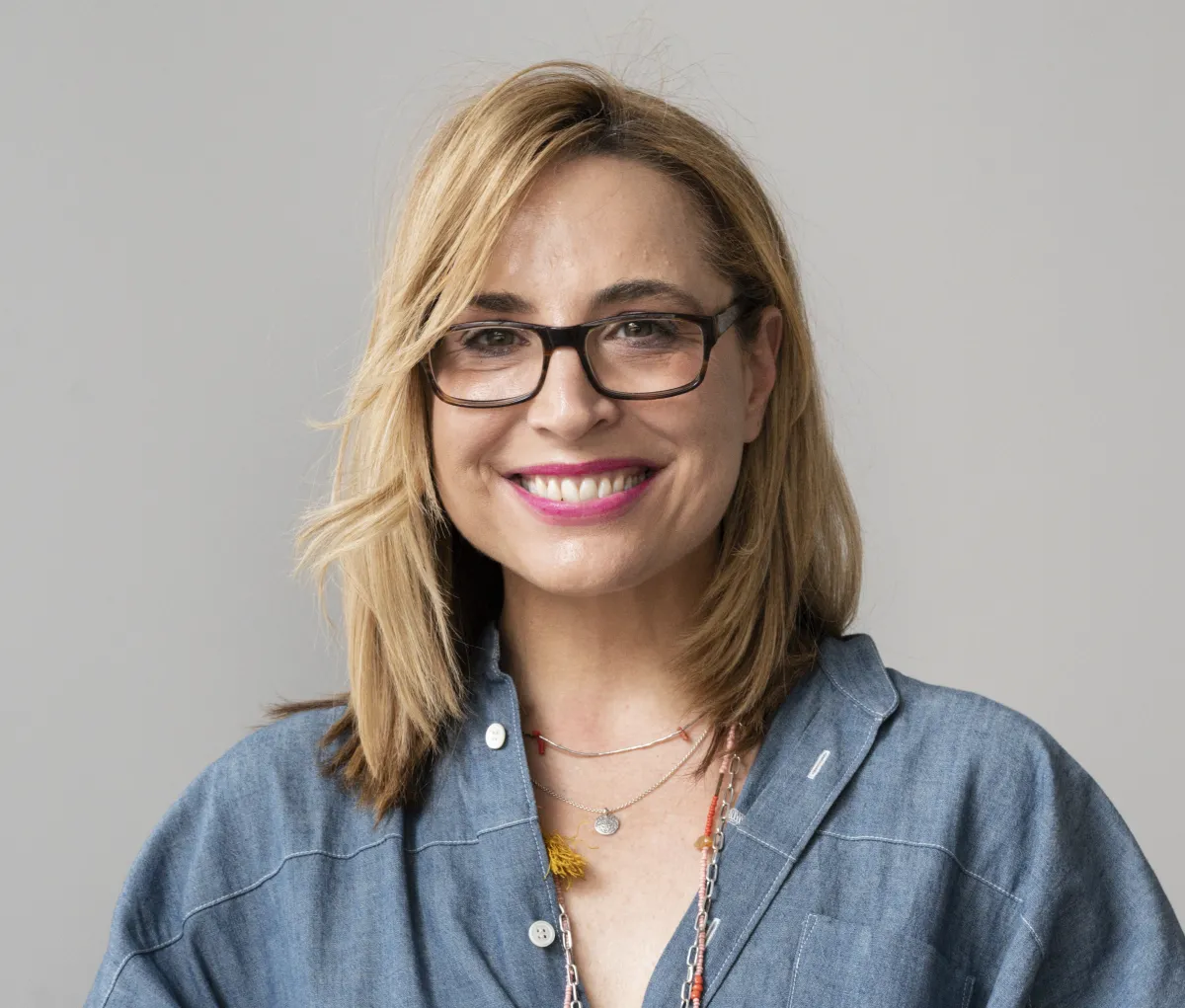 white woman with blonde hair and gkassess on grey background