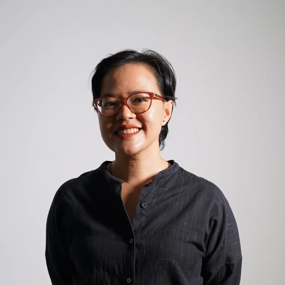 photo of an asian woman with short hair and glasses half of her face is shadowed 