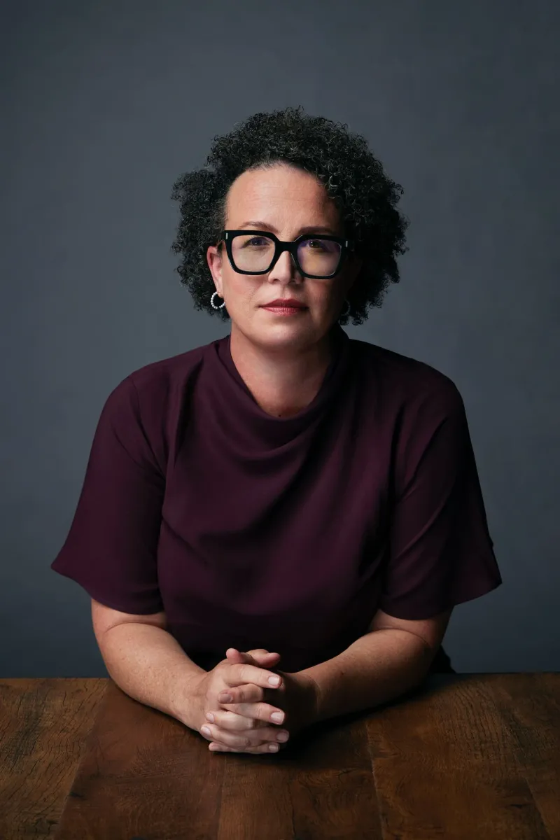 black woman with glasses and her hand folded over grey background