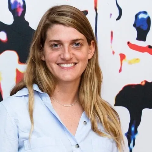 headshot of white woman with long blonde hair in front of a blurred abstract painting 