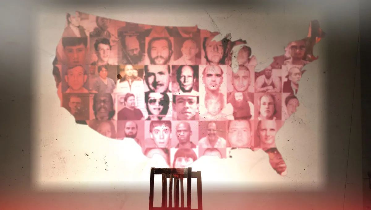 Map of the lower 48 states of the US projected on a wall with a chair in front of it.  Each state of the map has a mugshot or face of a mass shooter.