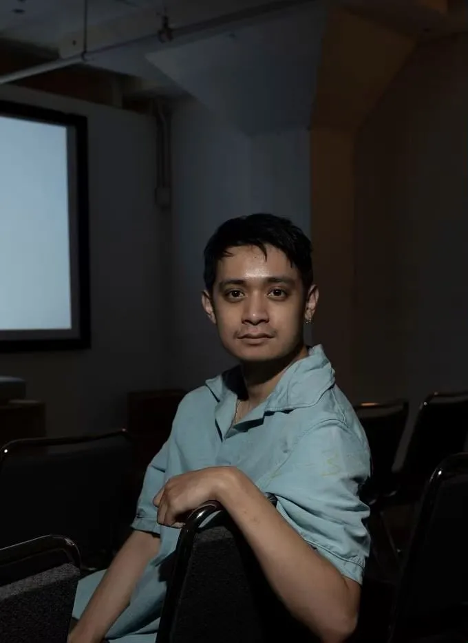 Headshot of Tony Nguyen. Asian person with short dark hair wearing a light blue button down shirt, sitting sideways in a black chair.