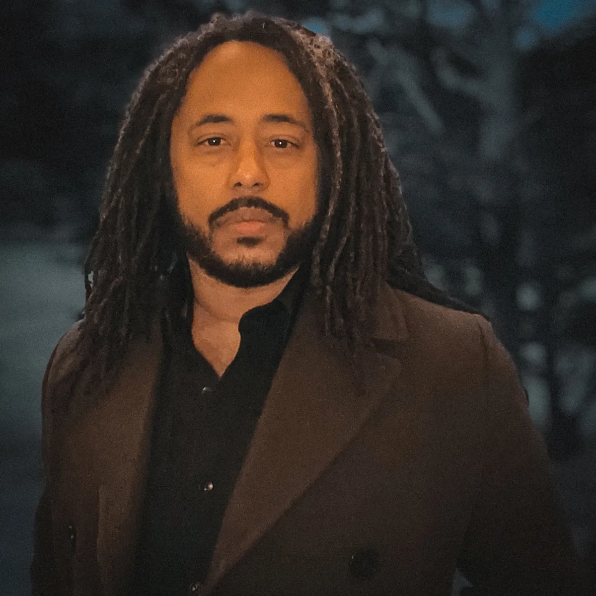 black man in brown suit and long hair over blurred background 