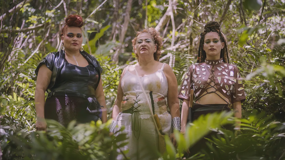 three people stand in a row in a jungle setting. they are wearing elaborate and beautiful outfits.