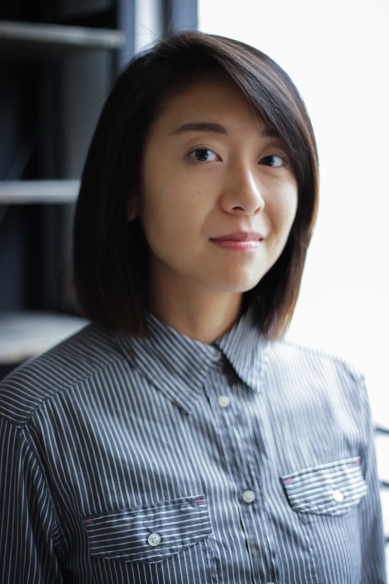 Professional headshot of asian person with a blue button up. their black hair swoops.