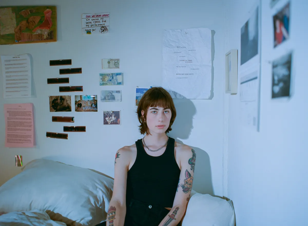 Headshot of an adult woman with light skin tone and shoulder-length brown hair, wearing a black tank top and reclining on a bed. General Title