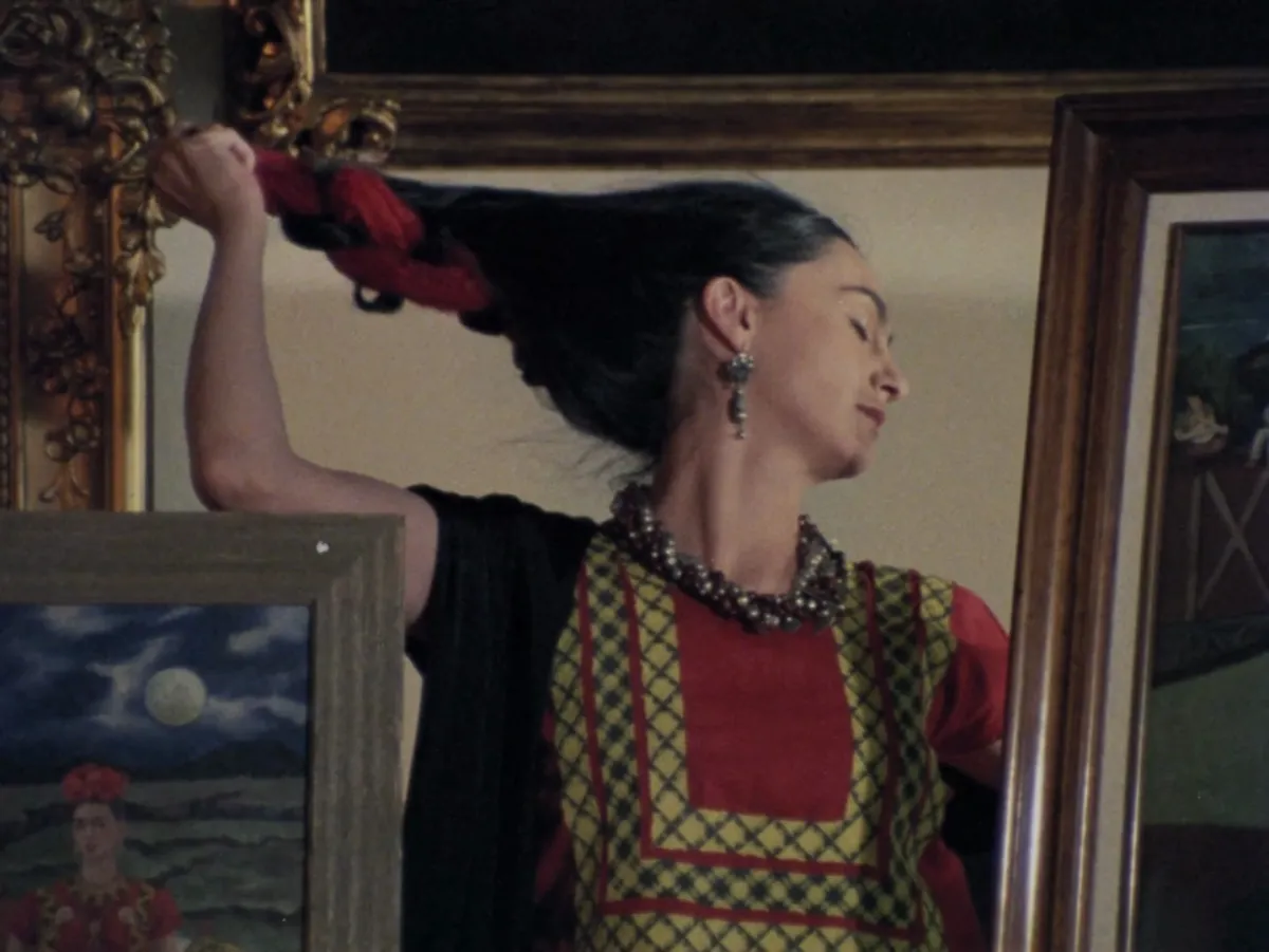 In a reflected mirror, a woman with long black hair removes a red hair ribbon.