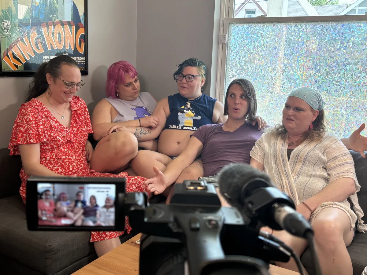 Five individuals sit on a couch in front of a camera