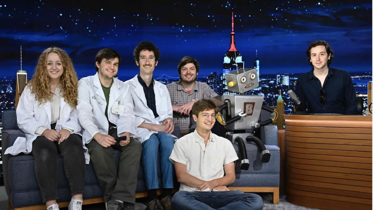 This is a group of friends sitting on a couch and floor at the tonight show. There is also a robot in the photo.