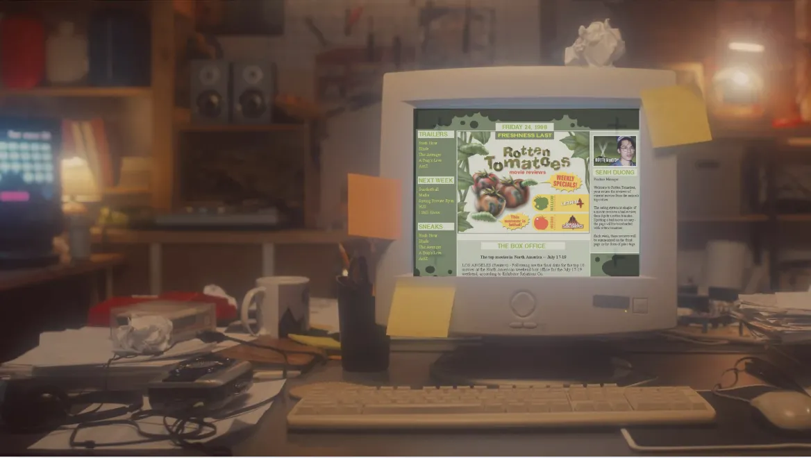 A bulky early 2000s computer displays the original Rotten Tomatoes homepage. It sits on a cluttered 1990s-style desk in a bedroom, surrounded by old tech, sticky notes, and personal items.