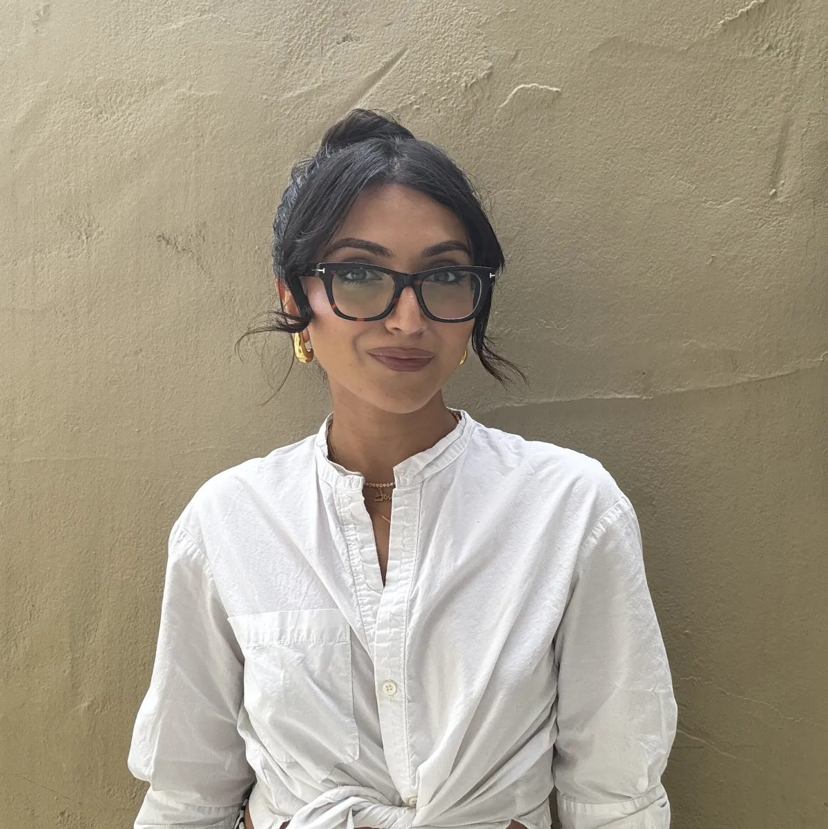 headshot of director wearing glasses in a white shirt in front of a concrete wall
