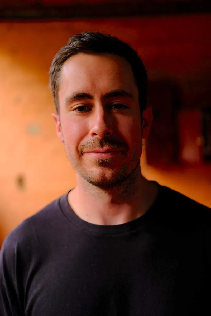 Headshot of a man with short hair wearing a dark T-shirt