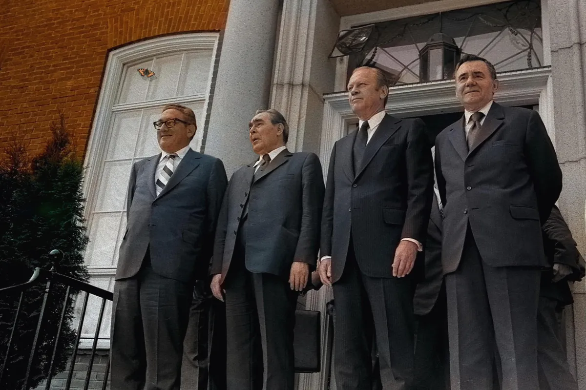 Four men in black suits stand in front of a grand entrance.