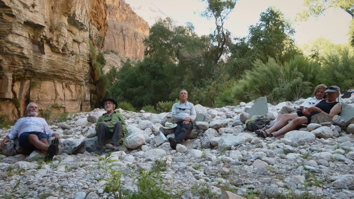 Five aging friends sit on rocks on the banks of the Colorado River.