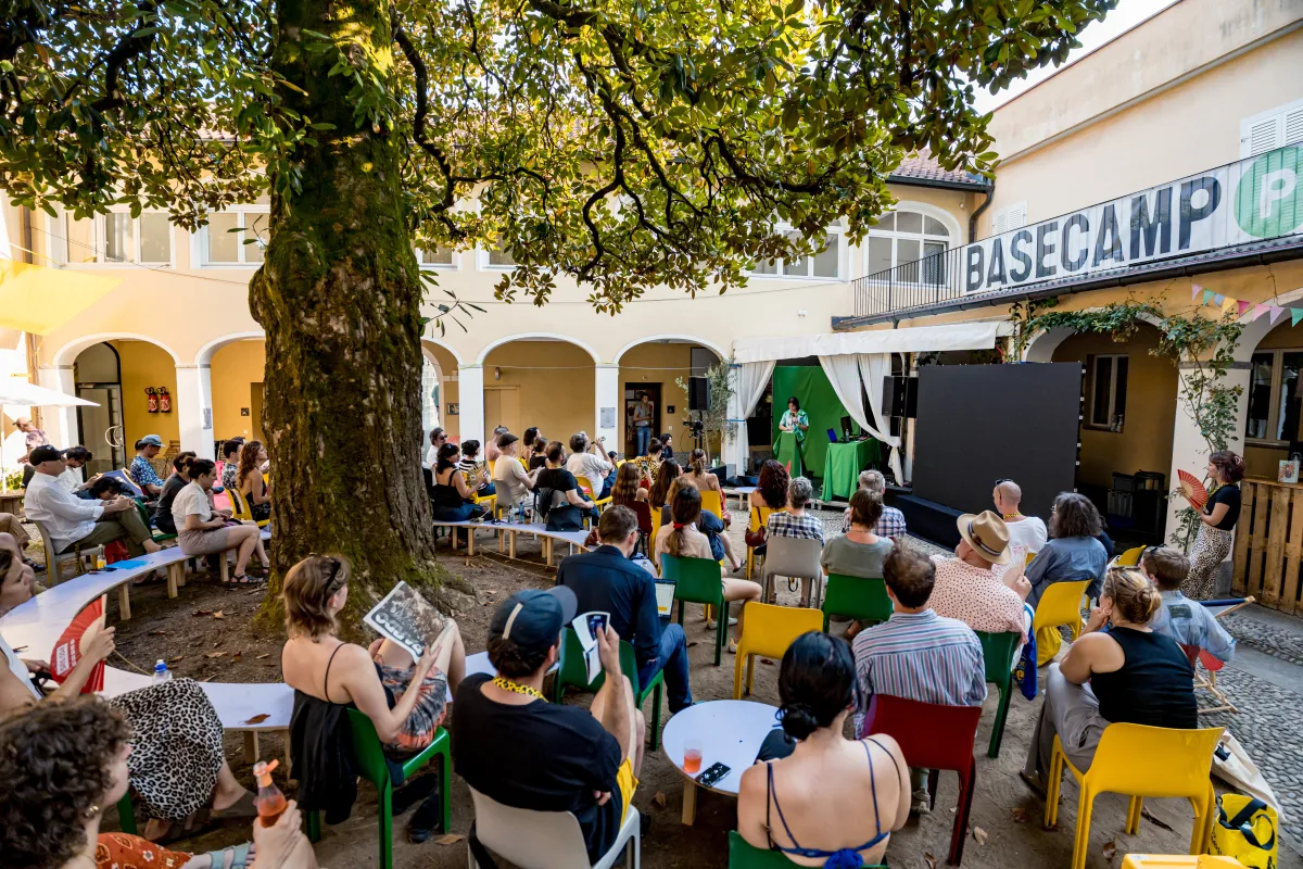 Attendees fill an outdoor courtyard, sitting around a large tree and under a banner that reads "Basecamp."