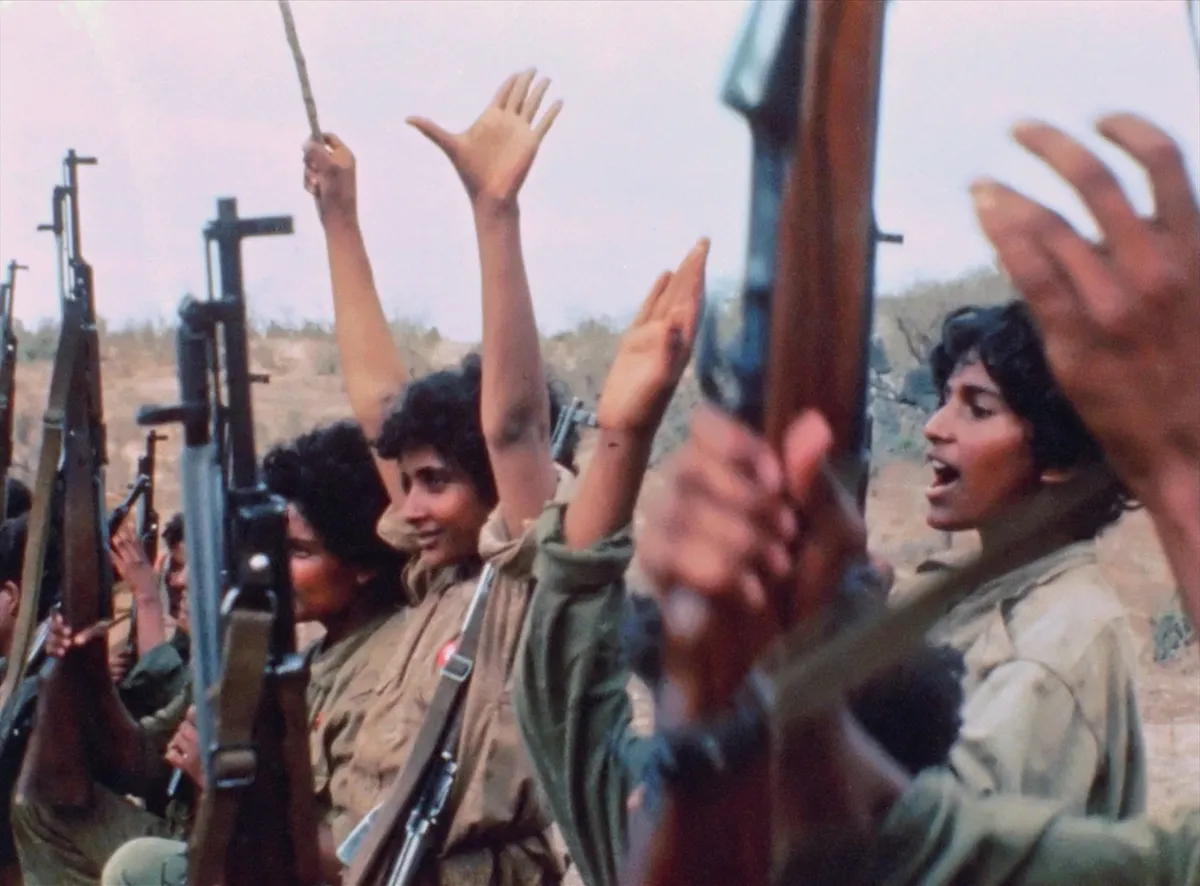 A row of young women with arms outstretched, brandishing rifles.