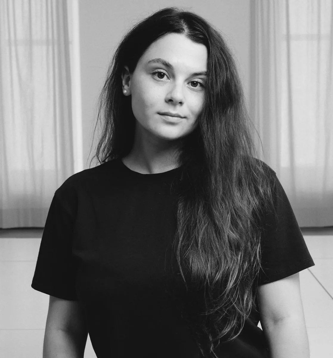 Black and white photograph of a young woman with long dark hair, wearing a black tshirt.