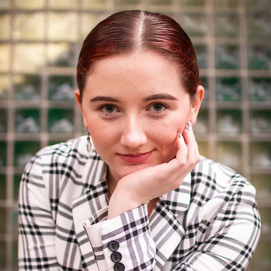 Headshot of a woman with slicked back hair and a plaid jacket.