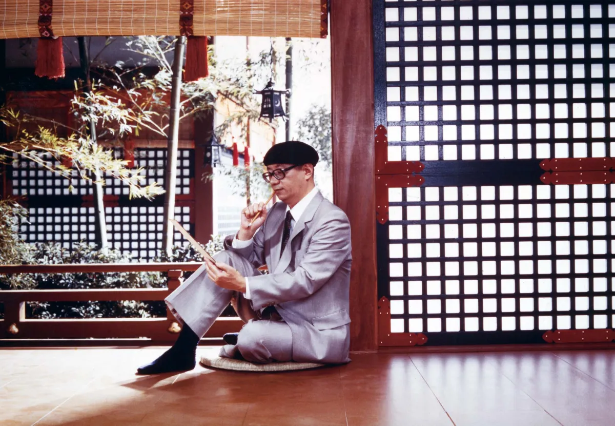 Osamu Tezuka (c. 1973) sits on the floor in a traditional Japanese room, observing a drawing, with a brush in his hand.