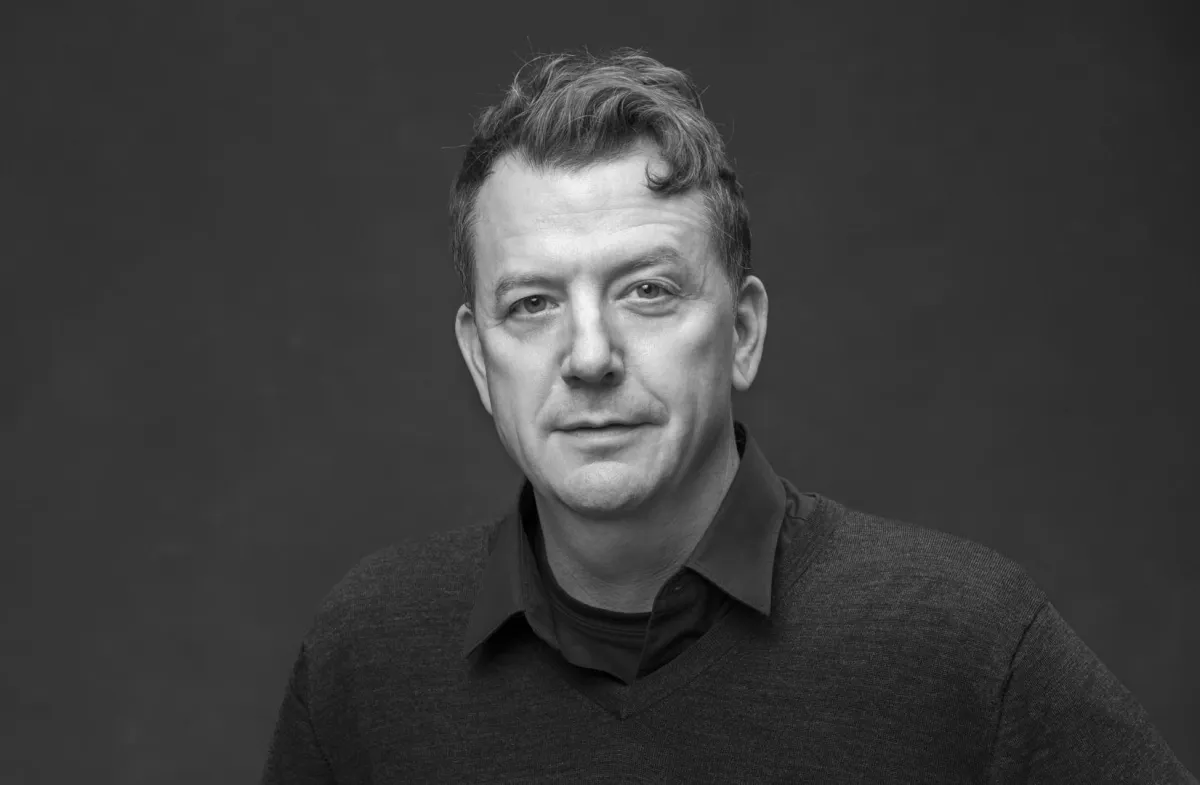Black and white headshot of a white man with nicely-cropped hair, wearing a shirt and a sweater.