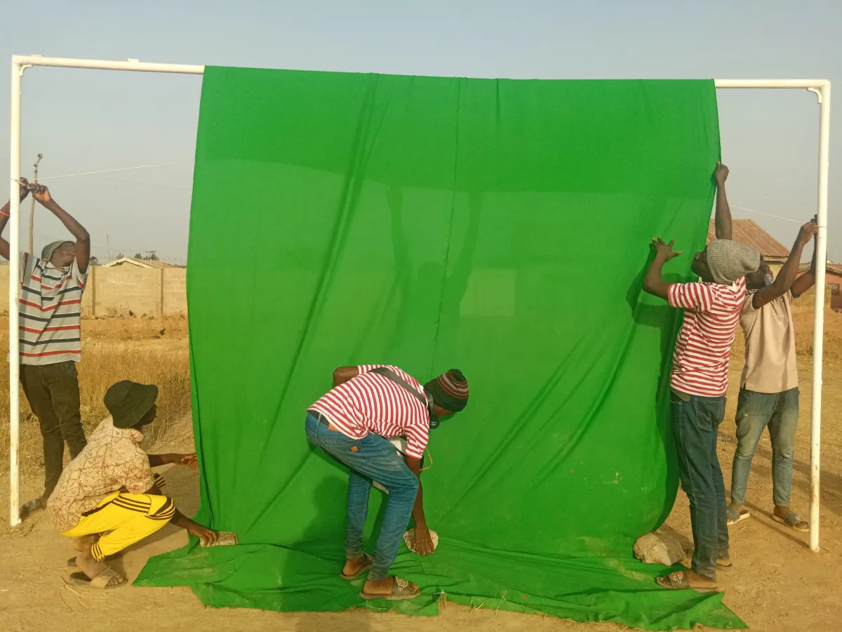 Five young Black kids in jeans and colorful shirts set up a green screen in the middle of a desert field