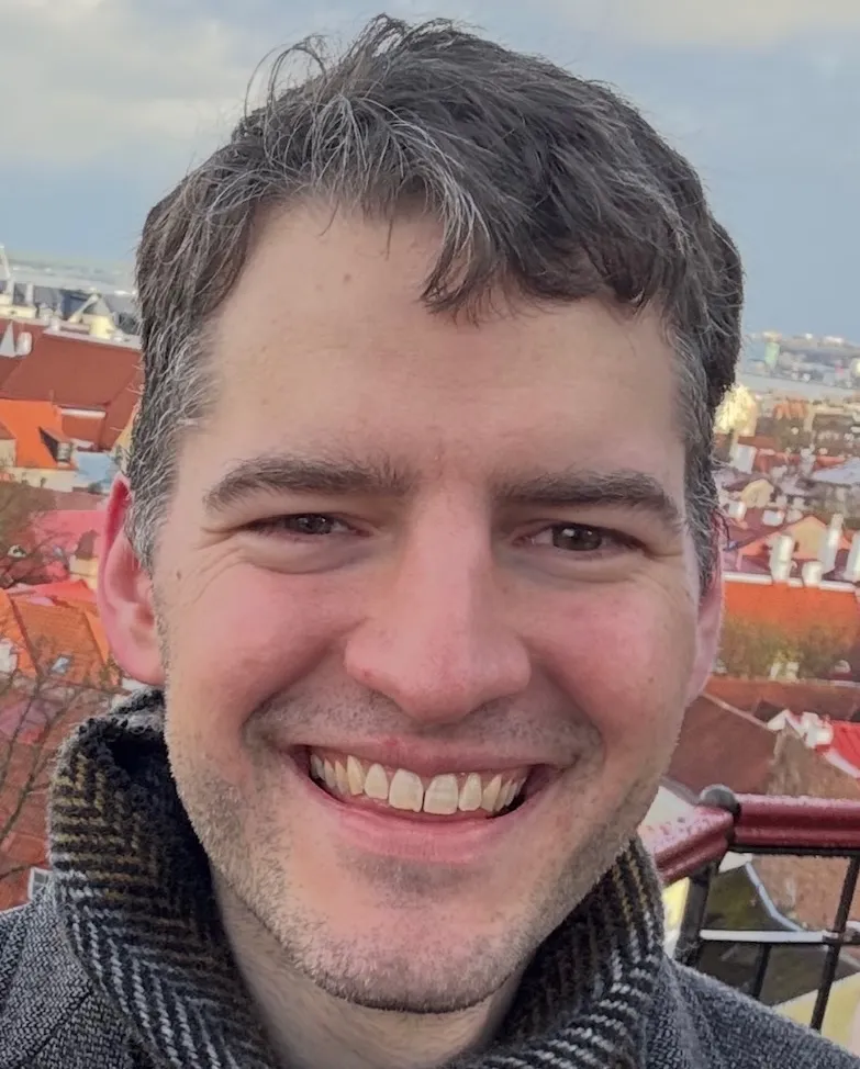 Headshot of a white middle-aged man with short greying hair in a scarf and a blazer