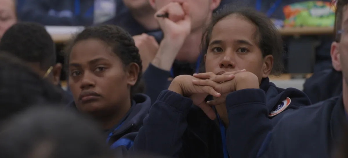 Two uniformed female guards sit next to each other in a classroom, surrounded by other uniformed guards