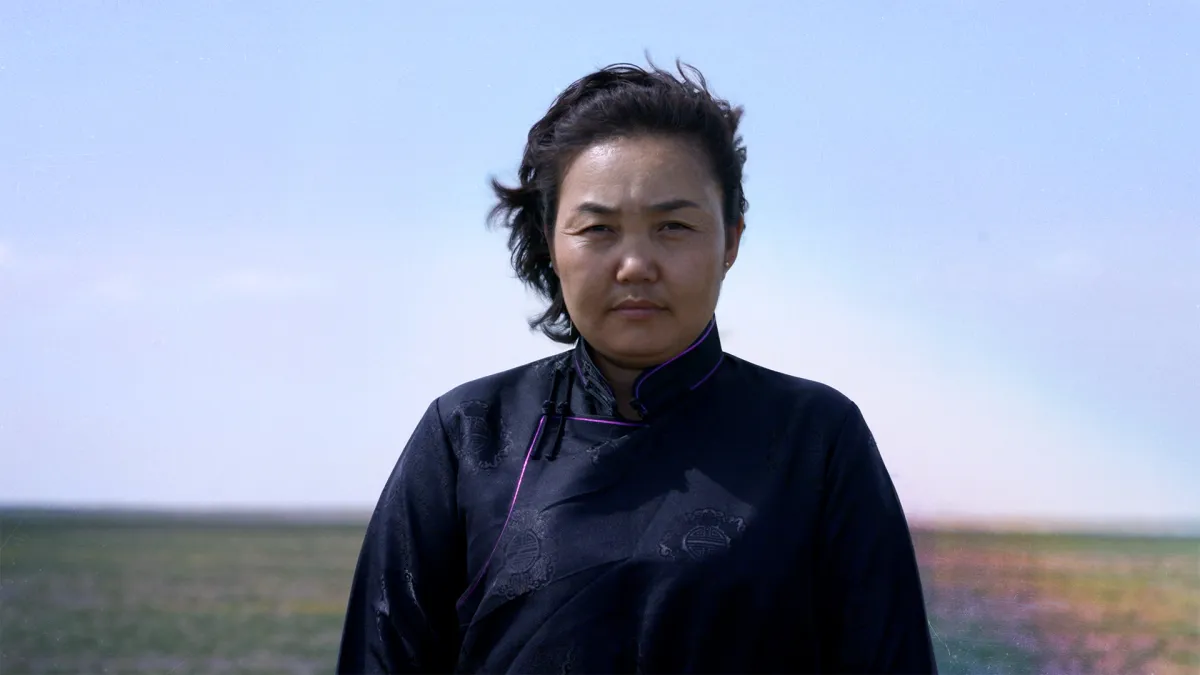 An Asian woman in a black top stares sternly into the camera, a blurred colorful field behind her