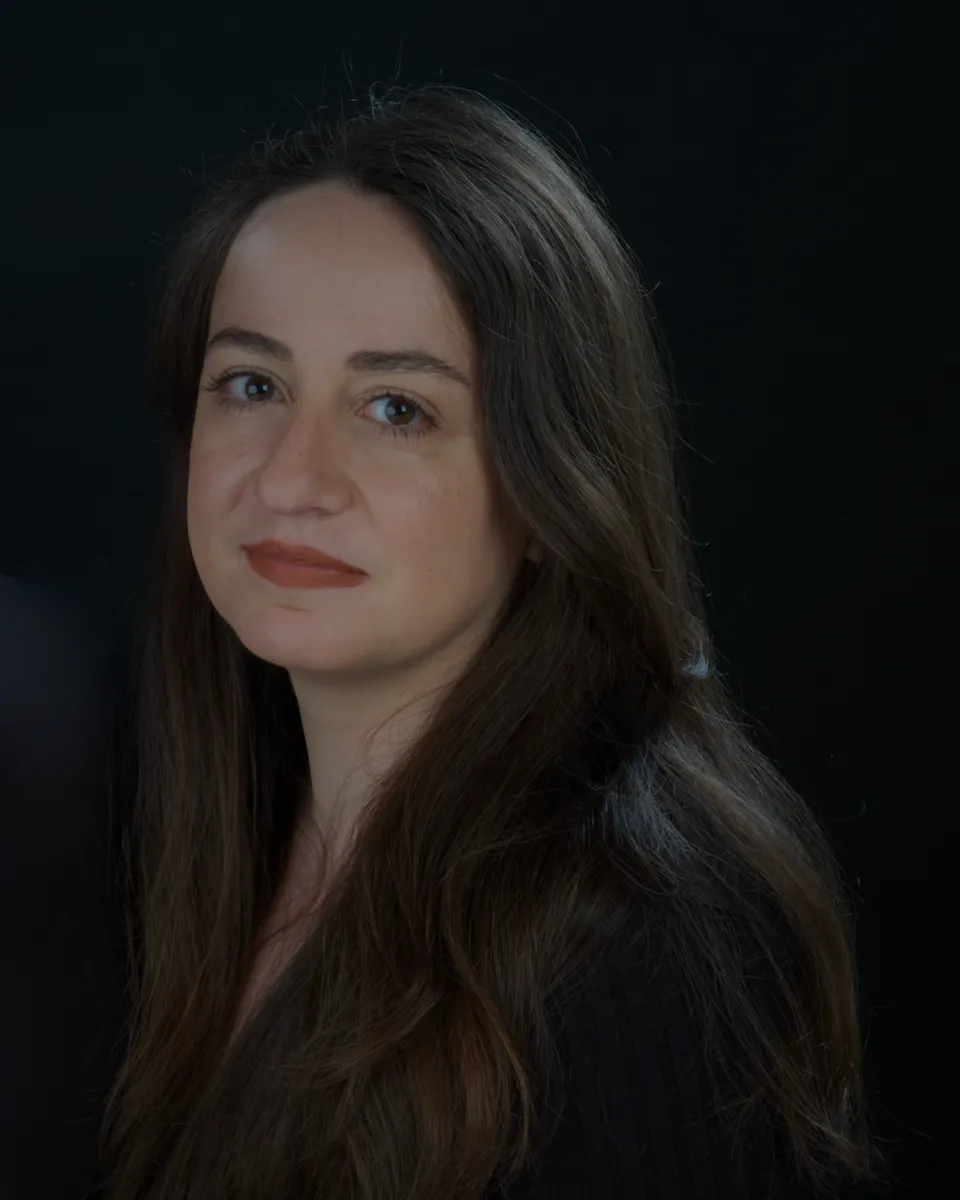 Headshot of a woman with long dark hair wearing a dark jacket in front of a black background