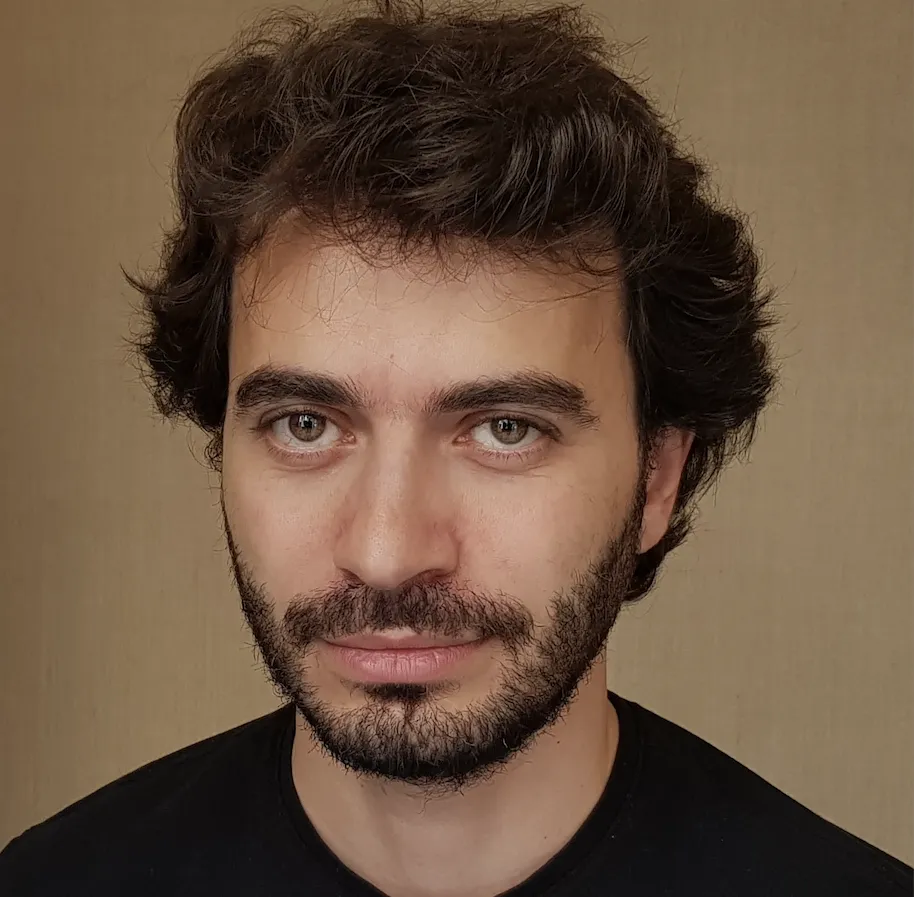 Headshot of a man with a dark beard and short hair wearing a black shirt against a brown background