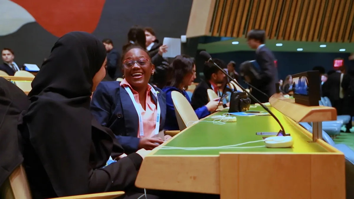 Two international high school delegates share a candid moment of laughter inside the United Nations General Assembly Hall during the WFUNA International Model United Nations conference. Surrounded by the iconic setting of global diplomacy, the image captures the intersection of youth, leadership, friendship, and cross-cultural connection that defines The Delegates.
