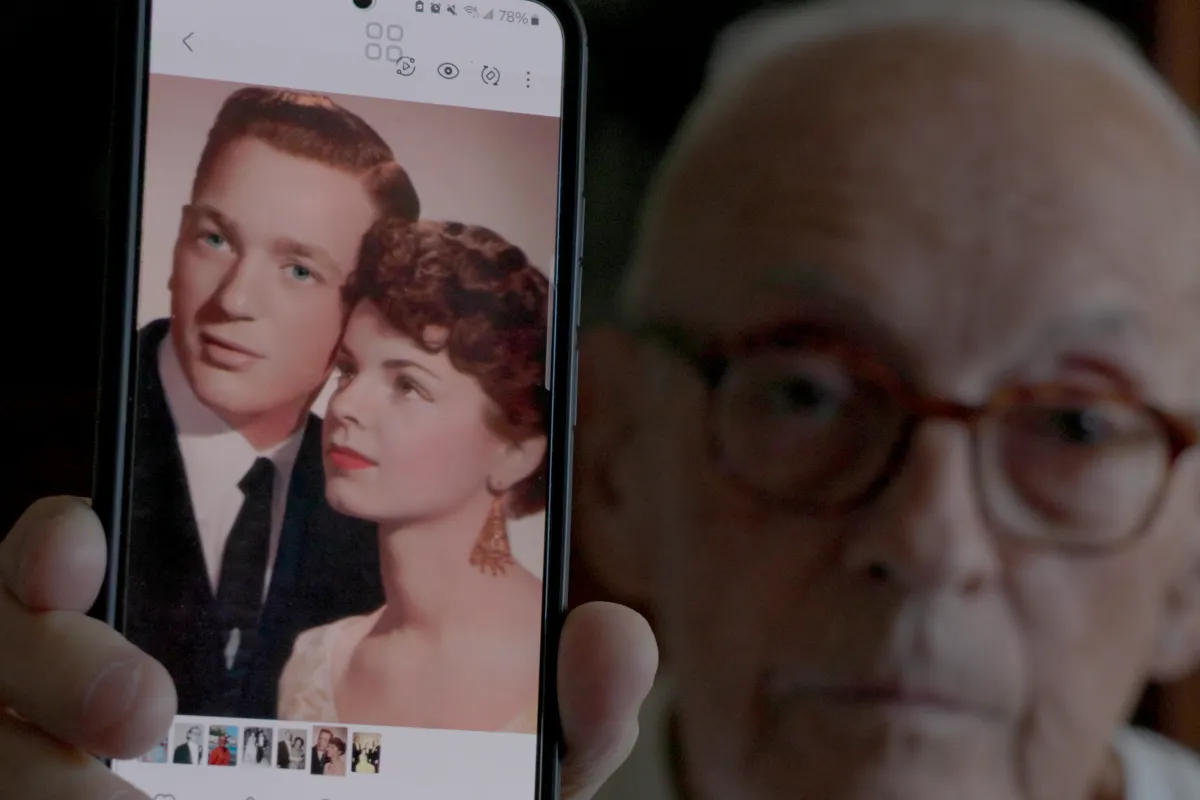 Man shows us a photo of two young lovers on his phone.