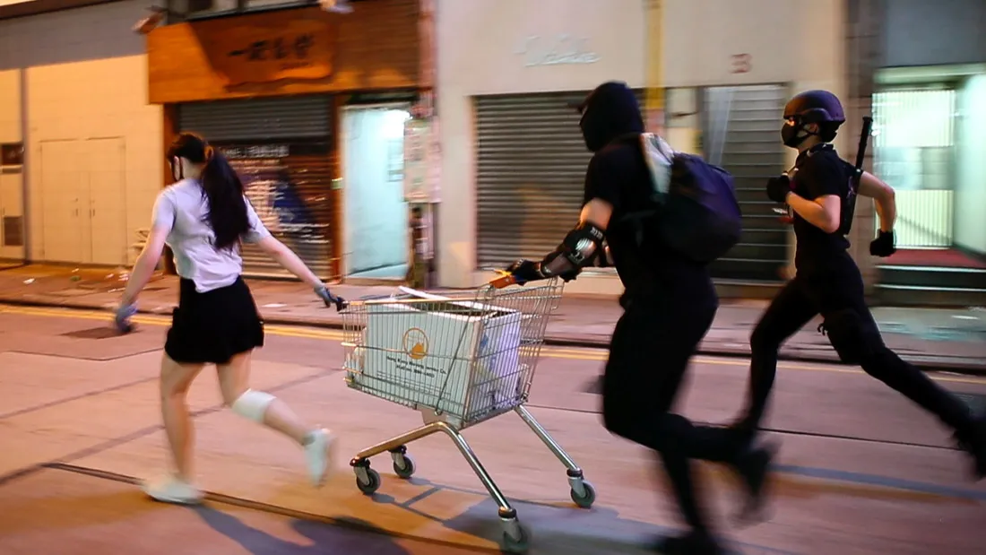 A still from 'Do Not Split', nominated for Best Documentary Short at the 93rd Academy Awards. The frame shows three young protestors in Hong Kong running down an empty street with a shopping cart.