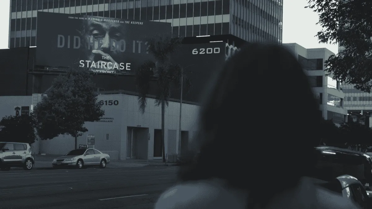 Margaret Ratliff is a white woman. Her back faces the camera as she looks at a billboard advertising the TV series ‘The Staircase.’ From Jennifer Tiexiera and Camilla Hall’s ‘Subject.’ Photo courtesy of Susan Norget Film Promotion.  