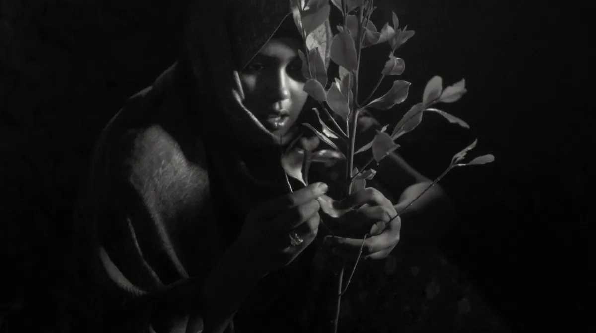 Black and white image of Habu Abdella, a young Ethiopian woman holding a stem of khat leaves. From Jessica Beshir's 'Faya Dayi.' Courtesy of Feyatey LLC