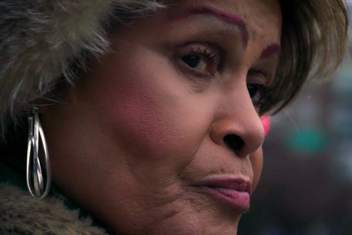 Close-up of Black trans woman, Gloria Allen, standing at a bus stop, wearing long oval silver earrings. Film still from Luchina Fisher's 'Mama Gloria'.