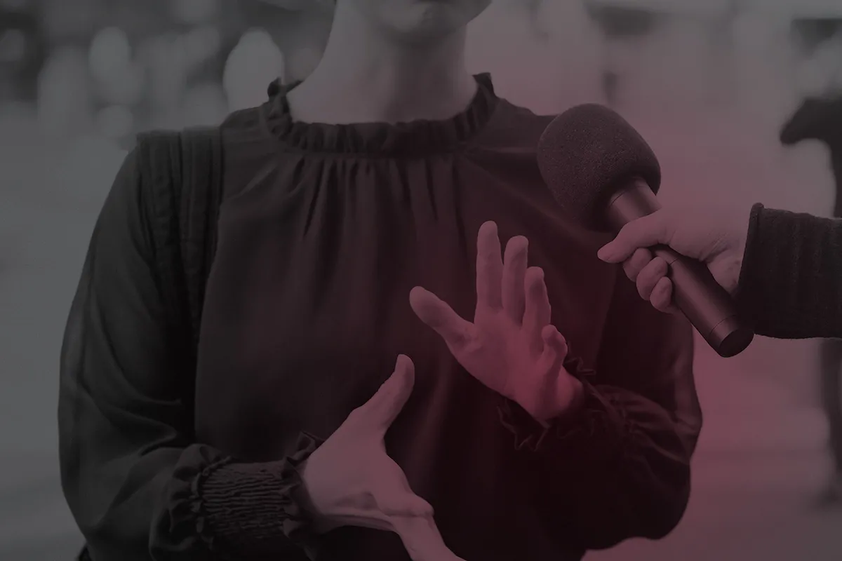 A picture of a person with light skin from chin down moving their hands. Another light skinned hand holding a microphone is facing this person.