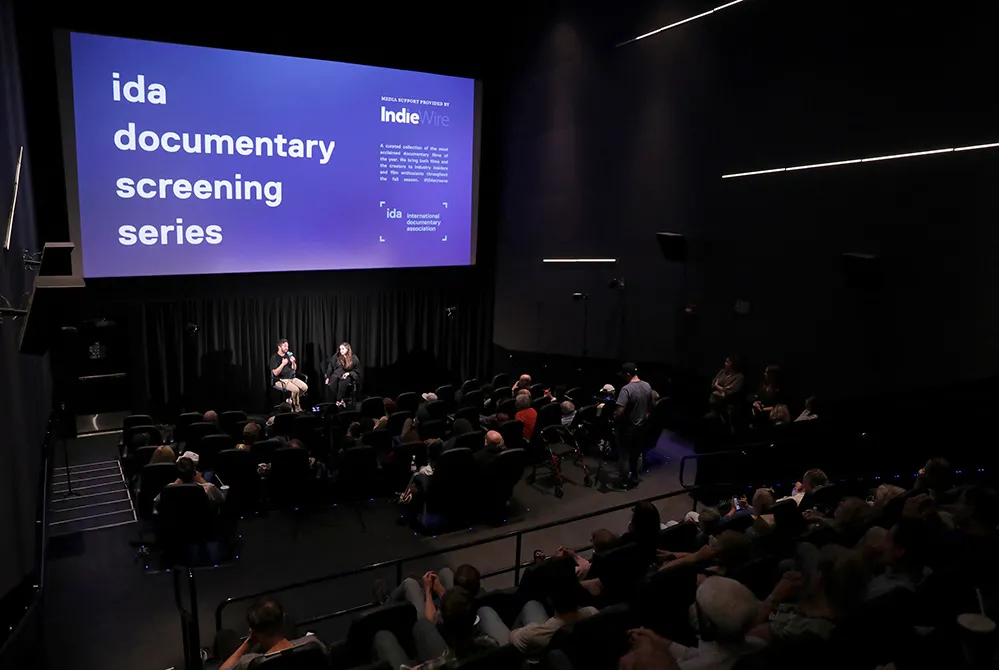 Two people sit in front of an audience. The projection behind them reads "ida documentary screening series." From a 2019 IDA Screening Series conversation with 'The Amazing Johnathan Documentary' team.