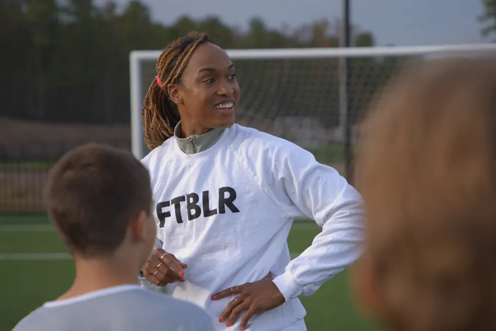 Soccer player Jessica McDonald is a Black woman in her 30s. Here, she is wearing a white shirt that says “FTBLR” and her hair is tied back. Image from Andrea Nix Fine and Sean Fine’s ‘LFG.’ Courtesy of HBO Max 