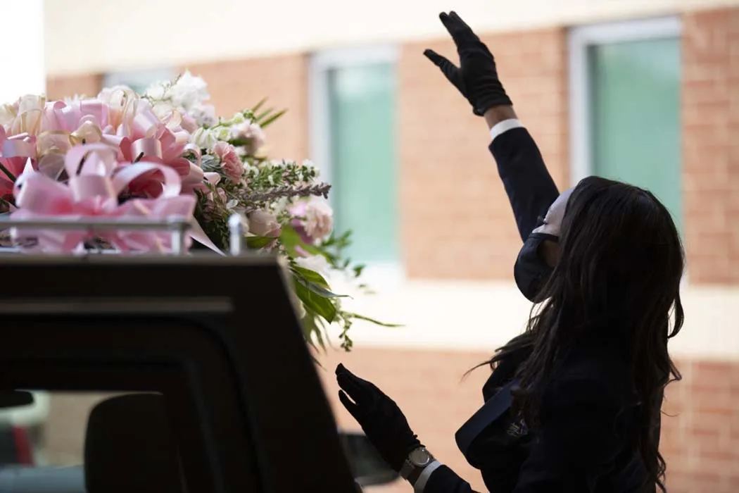 A masked Black woman funeral worker at a funeral at Franklin Avenue Baptist Church, New Orleans. She is standing next to a casket. From the 'Frontline' documentary ‘Death Is Our Business,’ directed by Jacqueline Olive. Courtesy of PBS Frontline.