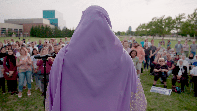 A woman wearing a hijab stands on a podium looking out at a crowd. Photo: Capital-K Pictures. Courtesy of POV.
