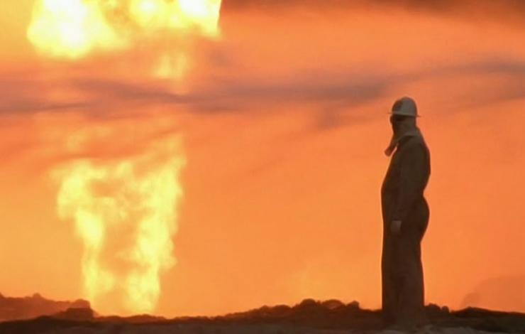 A person looks at a fire on the horizon, from Werner Herzog and Paul Berriff's 'Les­sons of Darkness.'