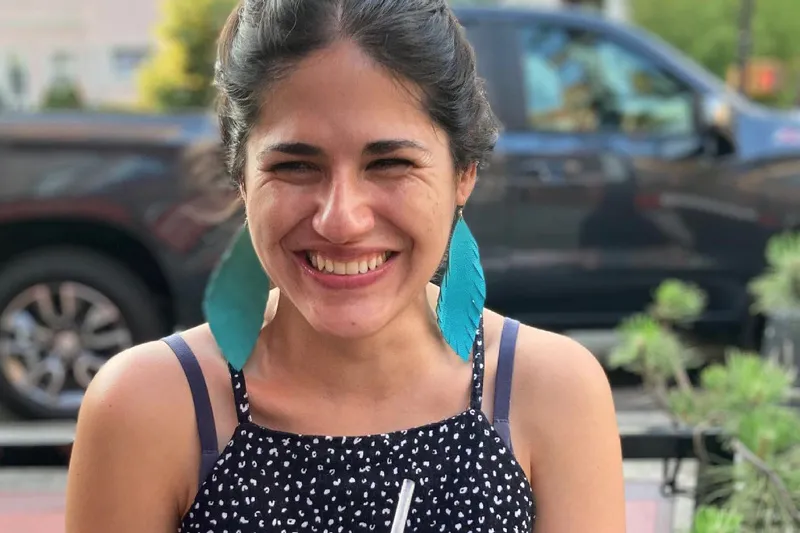 Mexican-American woman smiling with dark hair, wearing a black and white polka dot dress and teal earrings.