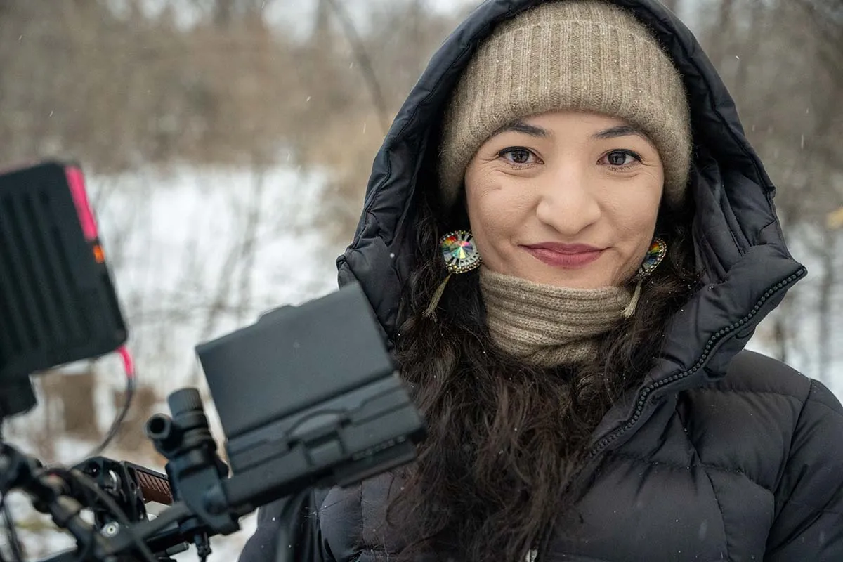 Tsanavi Spoonhunter is a Northern Paiute and Northern Arapaho woman with long, curly dark brown hair and eyes smiling into the camera.