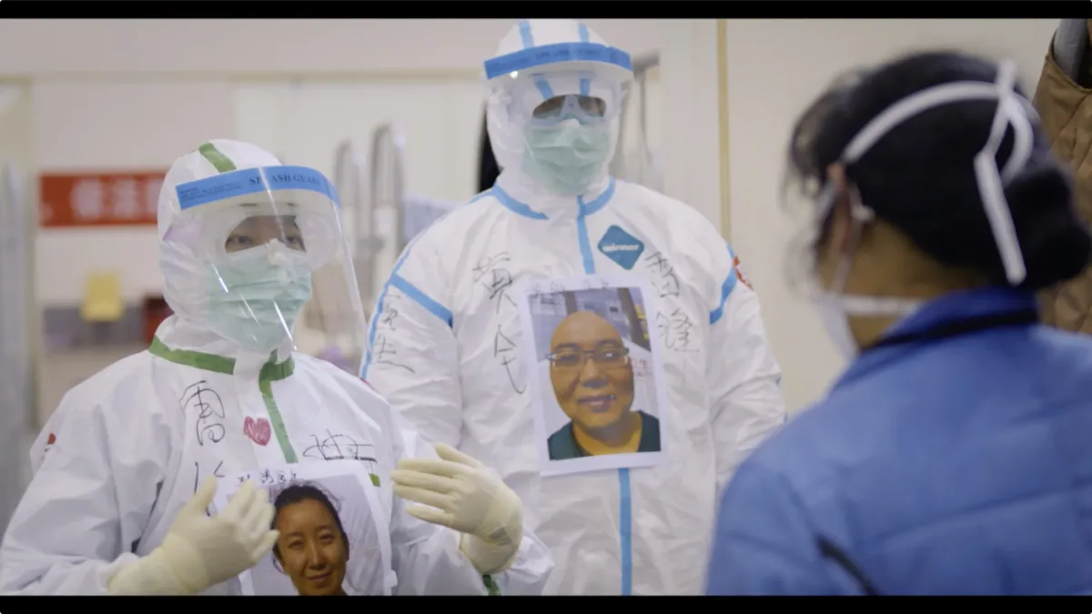 Two medical workers from Yung Chang’s ‘Wuhan Wuhan’ wear masks, bodysuits, and face shields with printed images of themselves on their chests in order to still be recognizable under all their safety wear. Courtesy of Stars Collective Films Entertainment Group Inc.