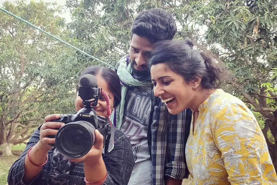 Three filmmakers from 'Writing with Fire' standing outdoors, smiling, looking at footage on a camera. 