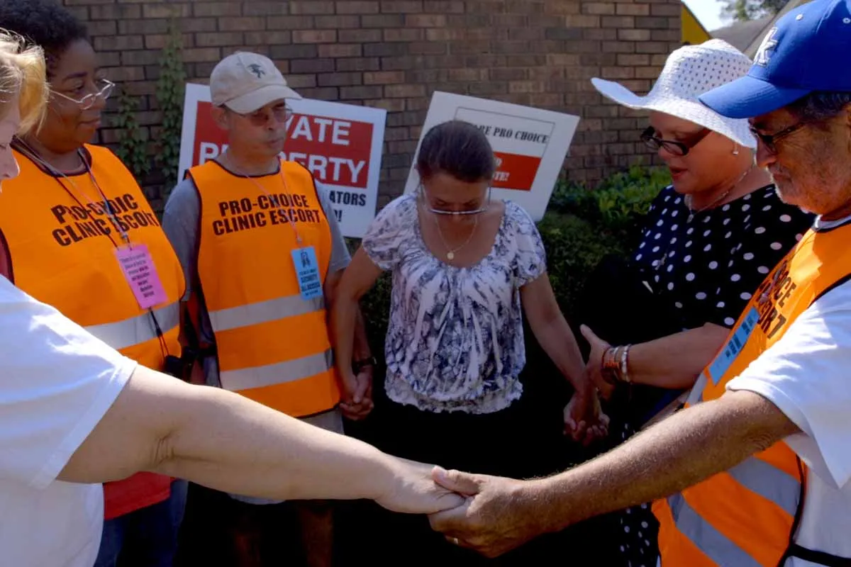 Pro-choice clinic escorts hold hands and stand in front of pro-choice posters, gathering to pray at Reproductive Health Services in Montgomery, Alabama. From Dawn Porter’s 'Trapped.' Courtesy of the film team.